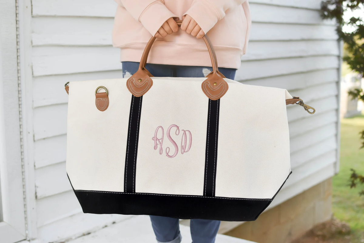 woman holding a large monogrammed canvas and black tote in front of her