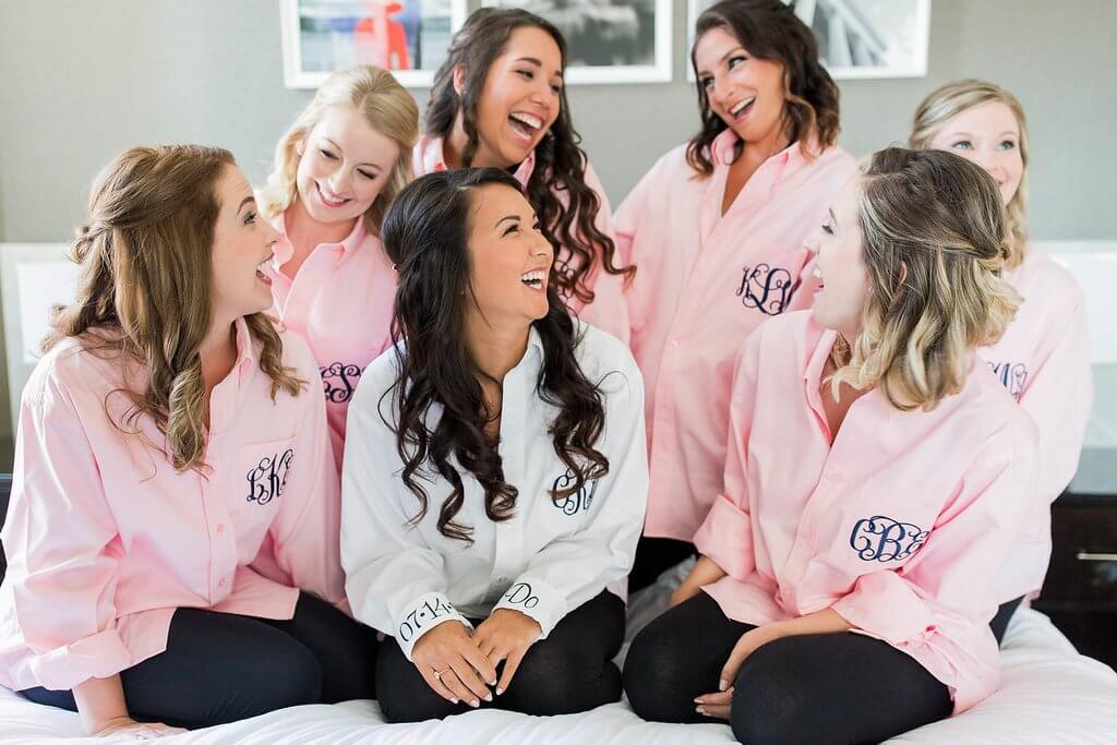 bride surrounded by bridesmaids dressed in pink button-up monogrammed shirts