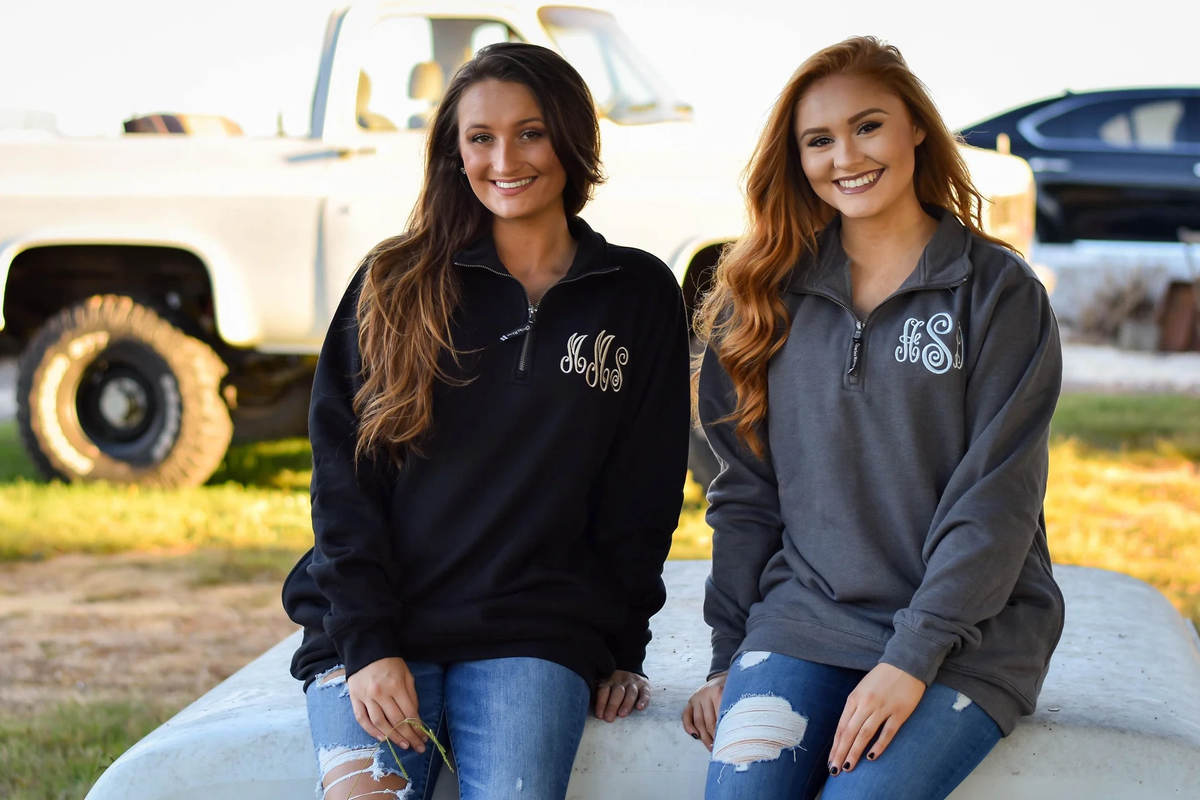 two women sitting together in zippered pullover sweatshirts with monograms